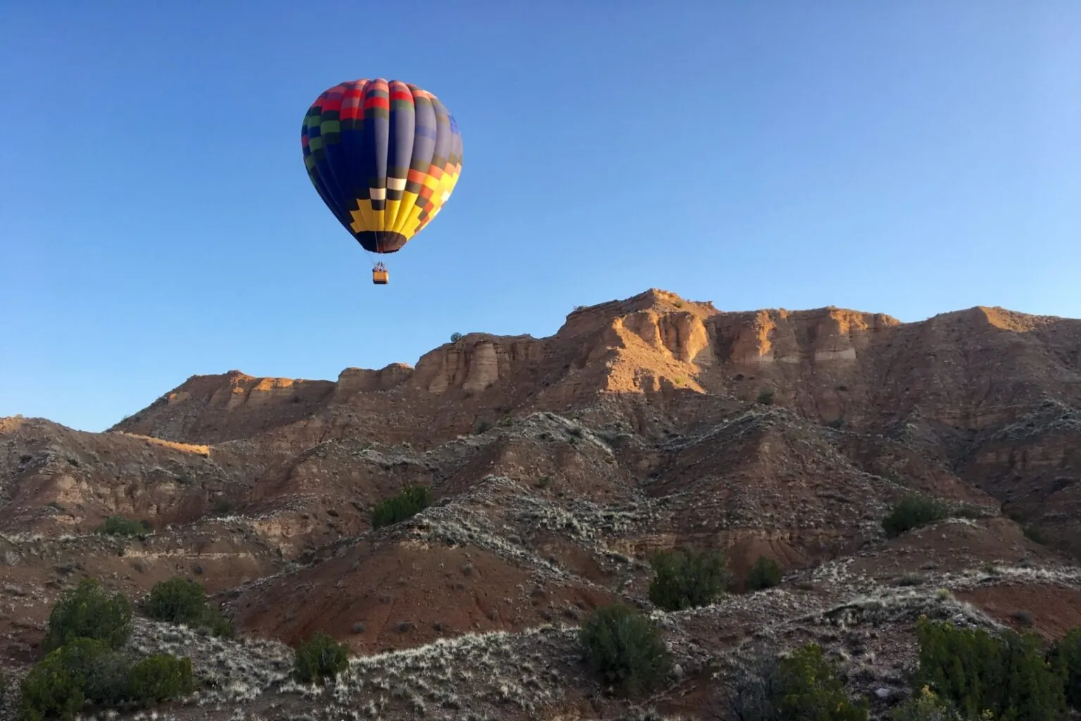 Hot air balloon flying over the red rock desert landscape of New Mexico during sunrise