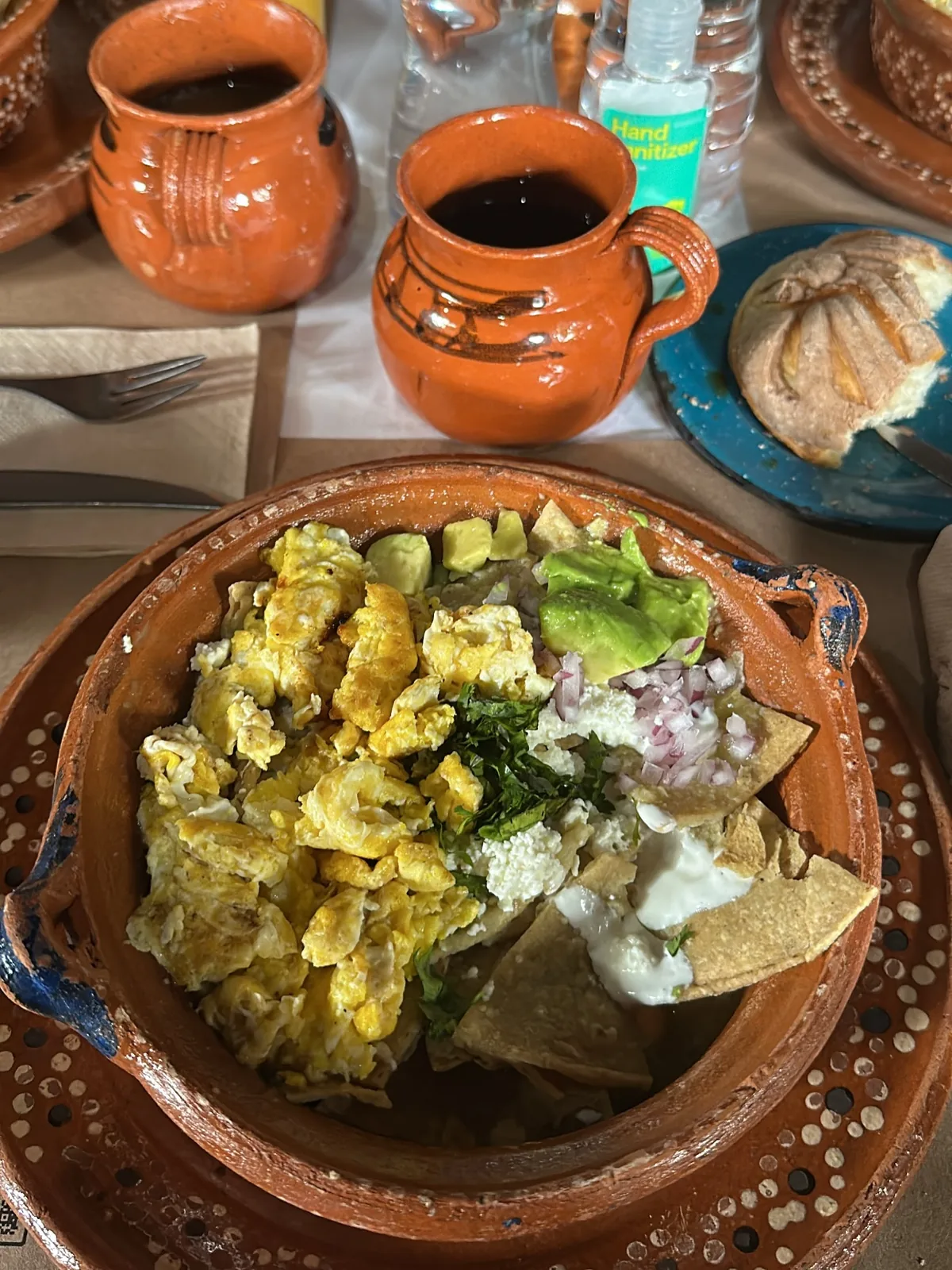 Desayuno de La Gruta Teotihuacán: huevos revueltos con chilaquiles, aguacate, queso fresco y crema en cazuela de barro, con café de olla en jarro y una concha