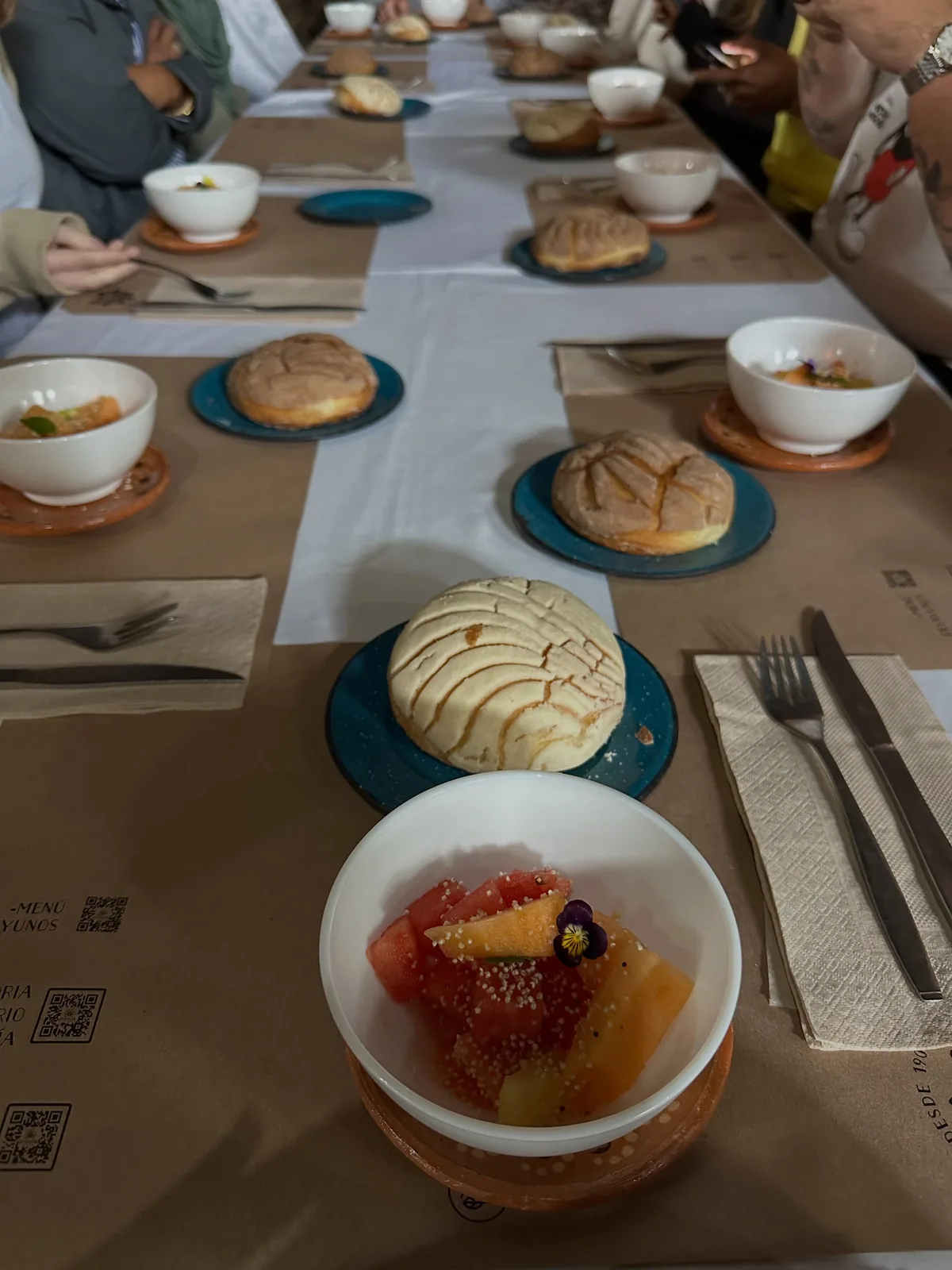 Mesa larga del comedor de La Gruta Teotihuacán puesta para el desayuno, con conchas, fruta de temporada con flor comestible y caldo en vajilla de talavera