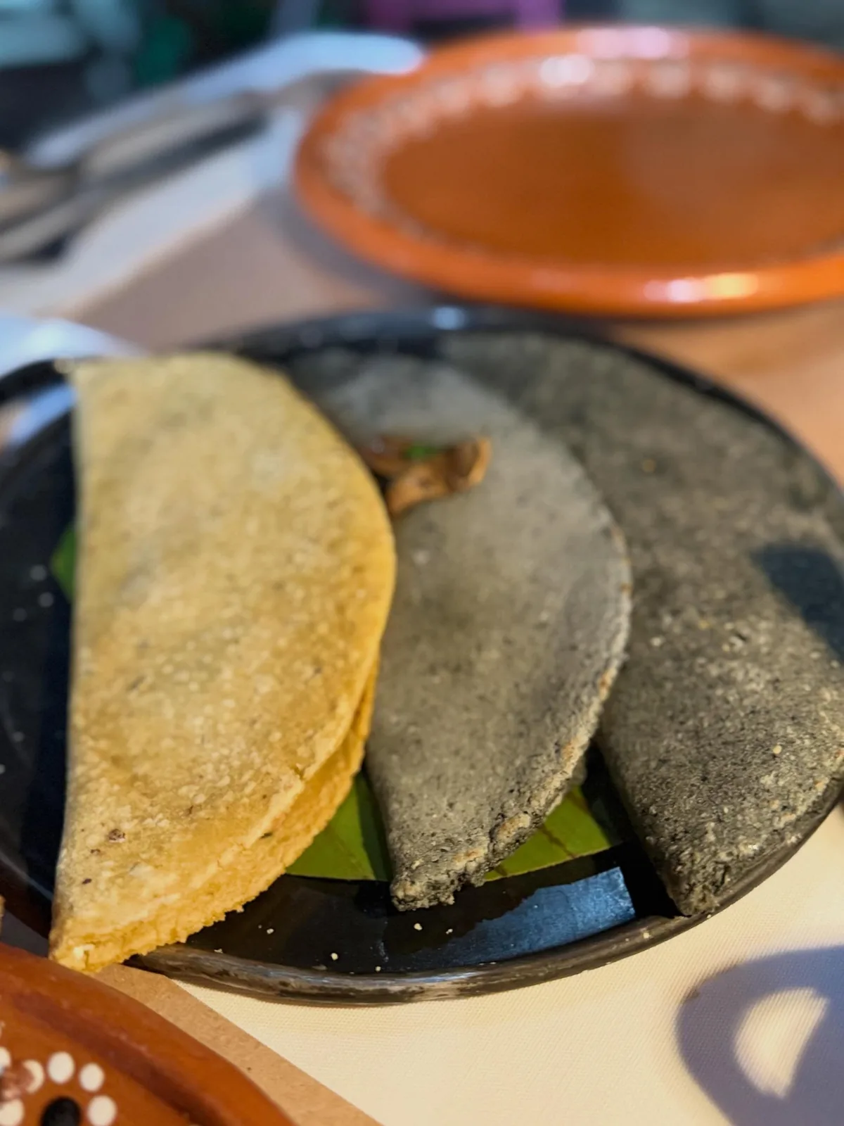 Dos quesadillas de La Gruta Teotihuacán, una de maíz amarillo y otra de maíz azul, servidas sobre comal de barro negro con hoja de plátano